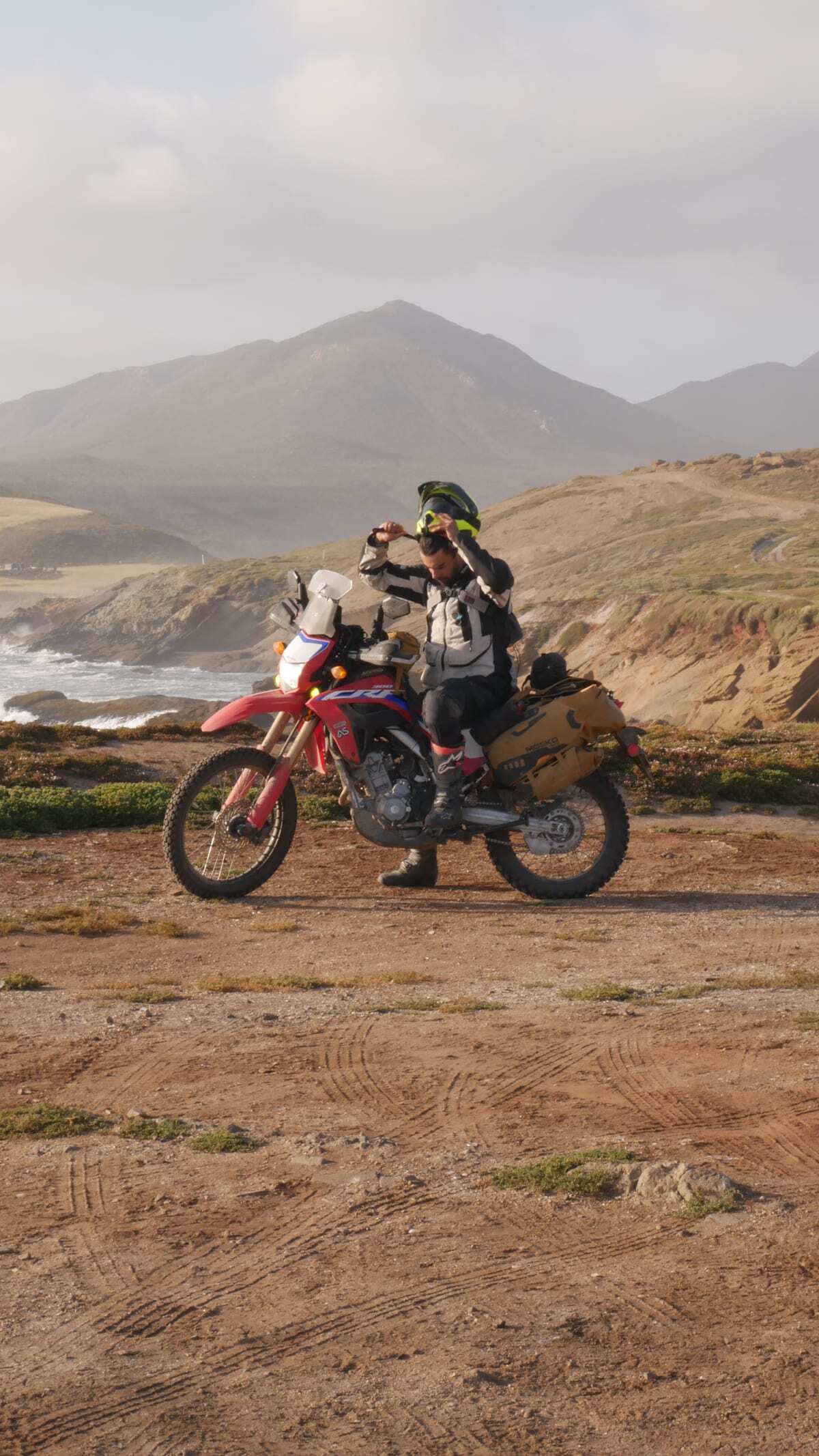 A rider removing his helmet beside his motorcycle on the Baja coast