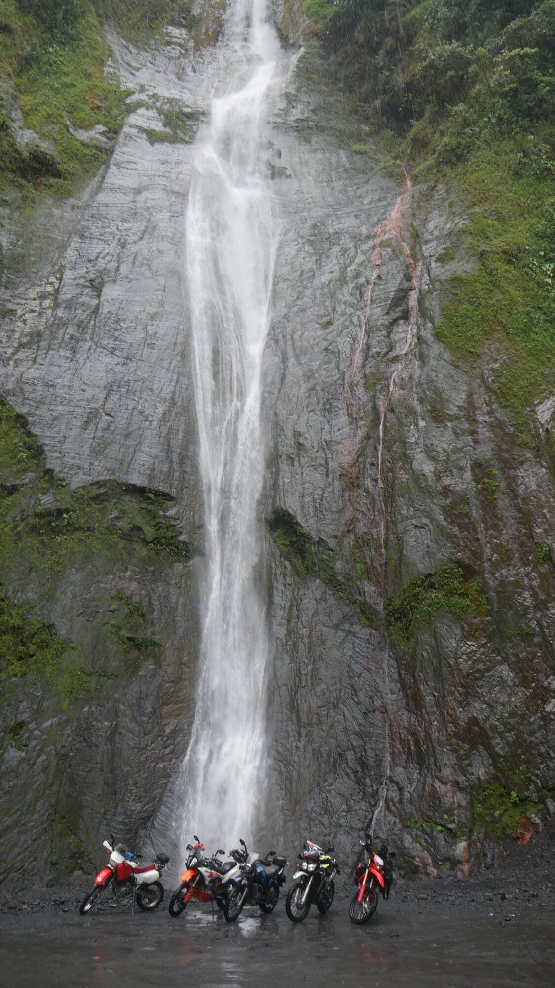 Motorcycles parked below a tall Colombian waterfall